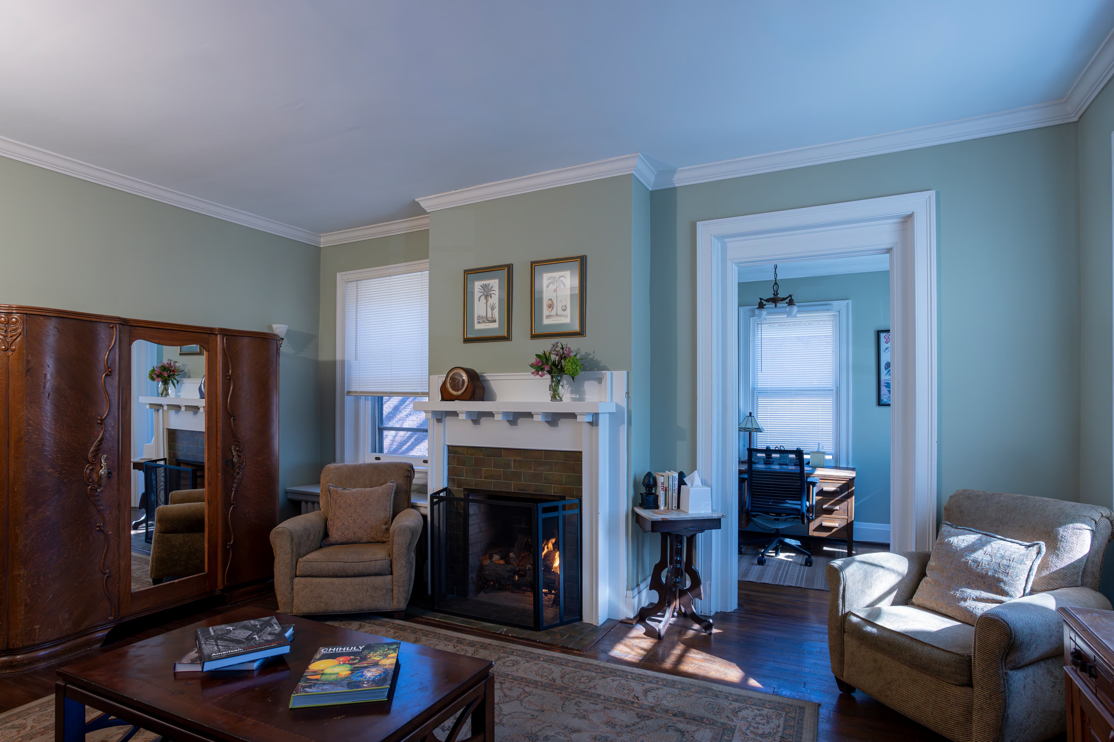 A living room with a fireplace, two armchairs, a television, and light green walls.