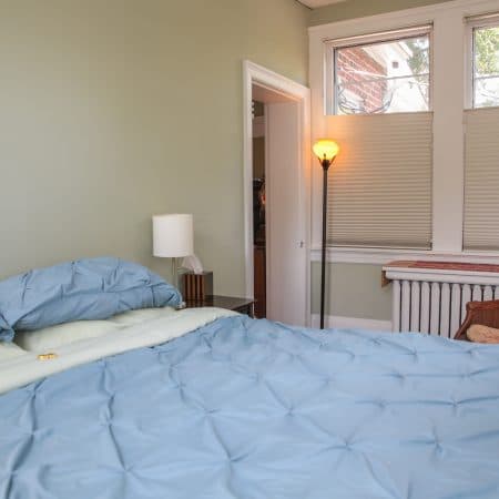 A bedroom with light green walls, a bed with blue bedding, and a large window.