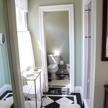 A bathroom with light green walls and black and white checkerboard floor tiles, leading into a smaller powder room.