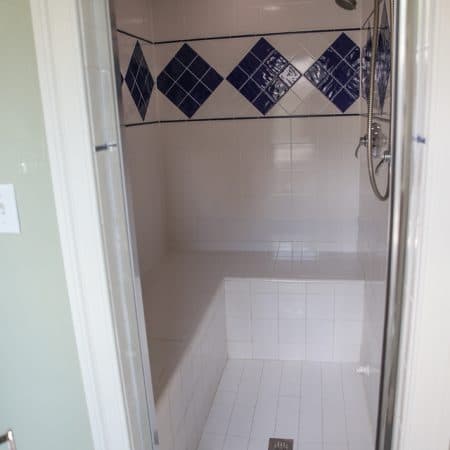 A white-tiled shower with a diamond pattern of blue tiles.