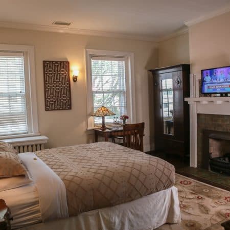 A cozy bedroom with a queen bed, a fireplace, a TV, and a dark wooden armoire.