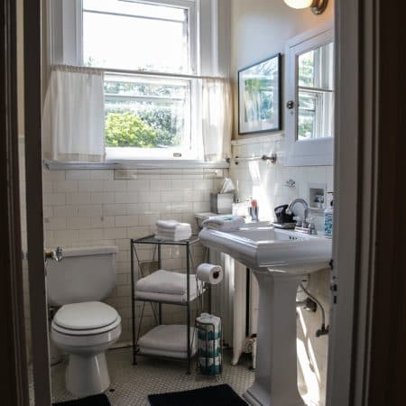 A small half-bathroom with a white pedestal sink and toilet, with white bathrobes hanging in the doorway.