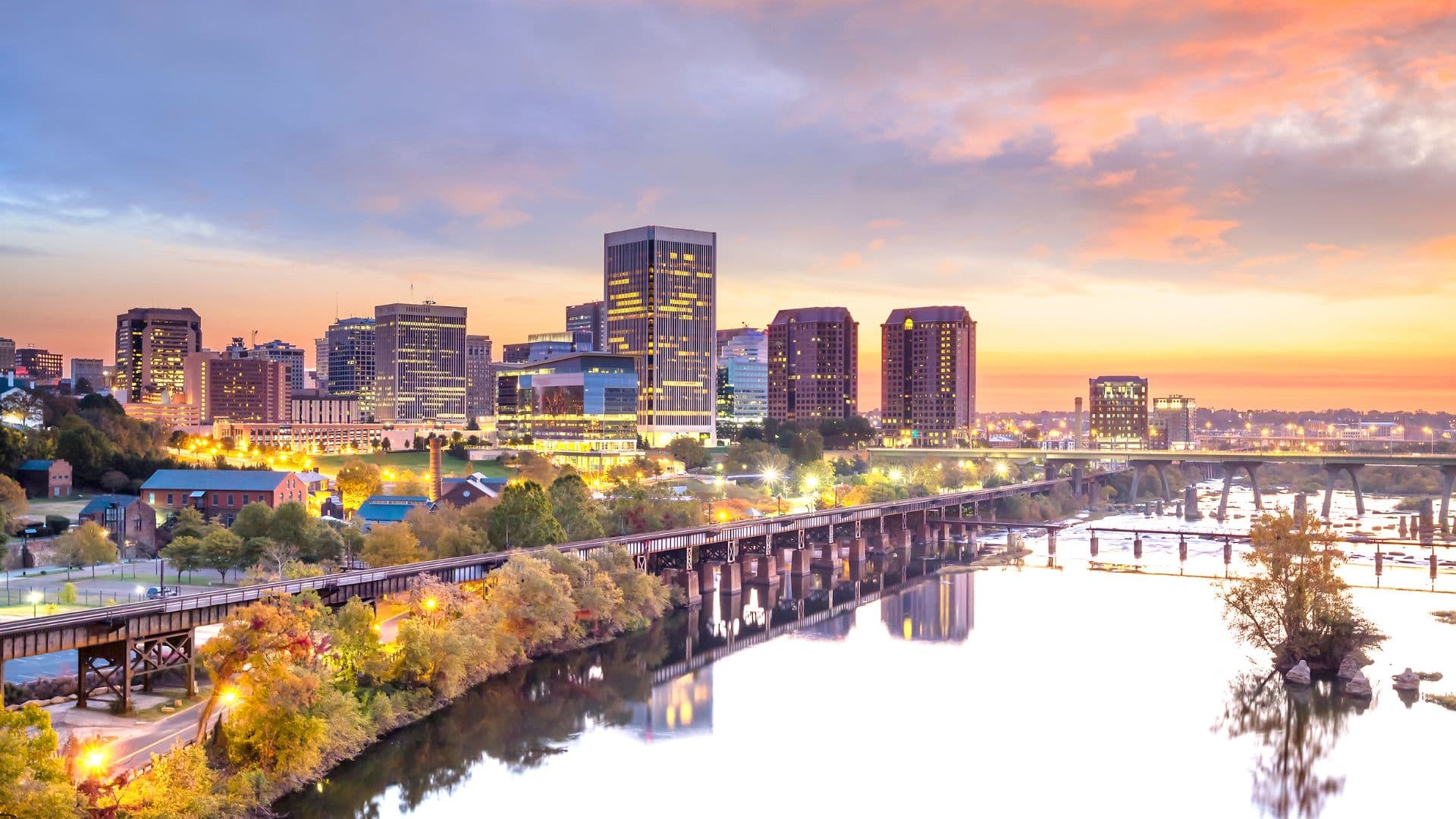 A skyline view of a city at sunset with reflections in the river and bridges.