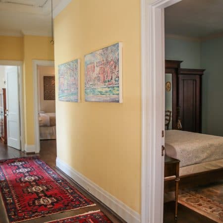 A bright yellow hallway with a red patterned runner rug and two framed artworks, leading to other rooms.