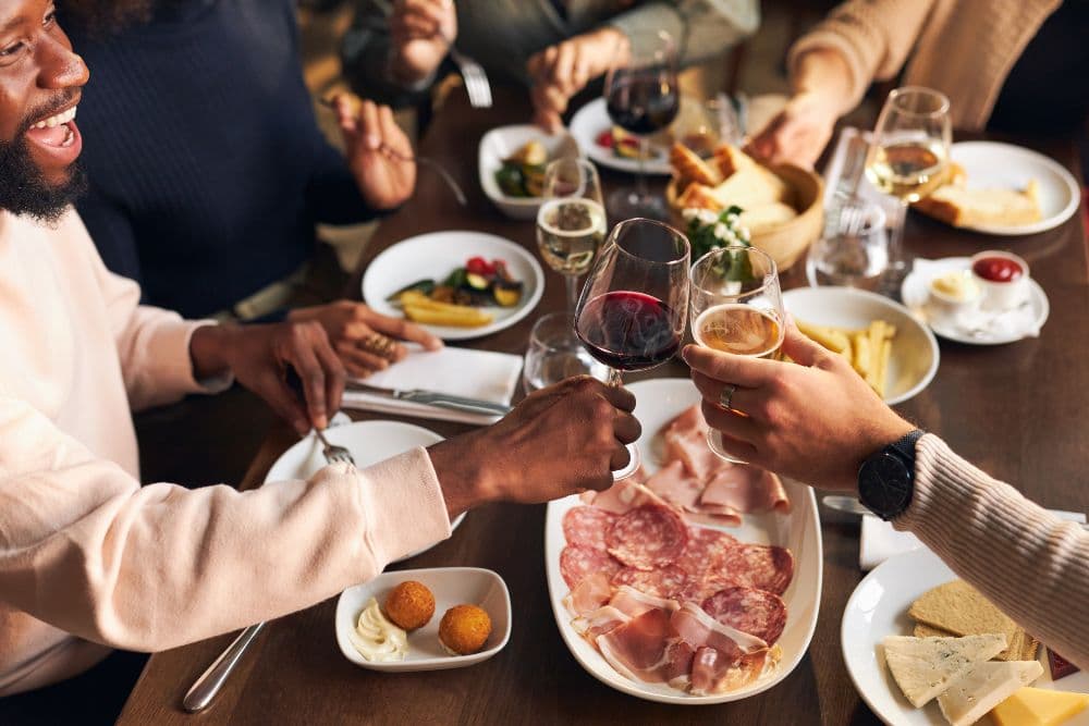 A diverse group of friends toasting with wine glasses over a table filled with food.