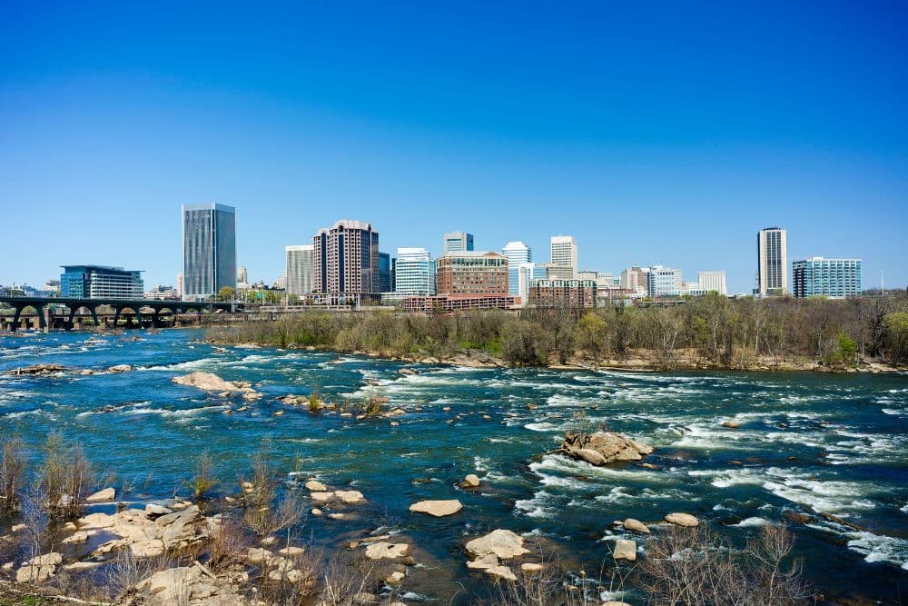 A vibrant city skyline overlooks a flowing river under a clear blue sky.