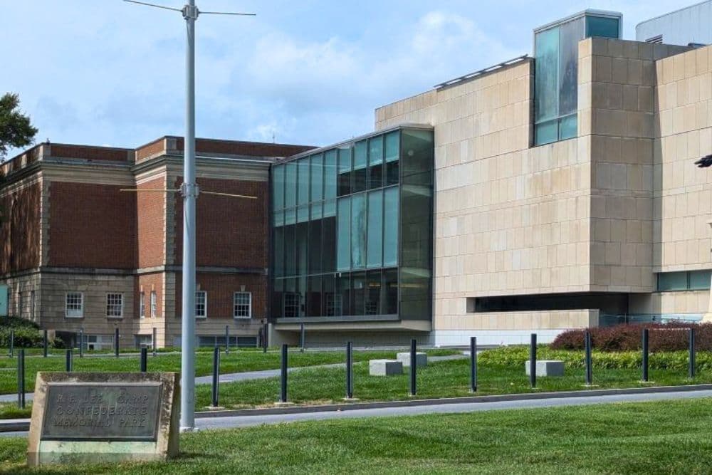 Modern building with glass features adjacent to a brick structure, set in a green landscape.