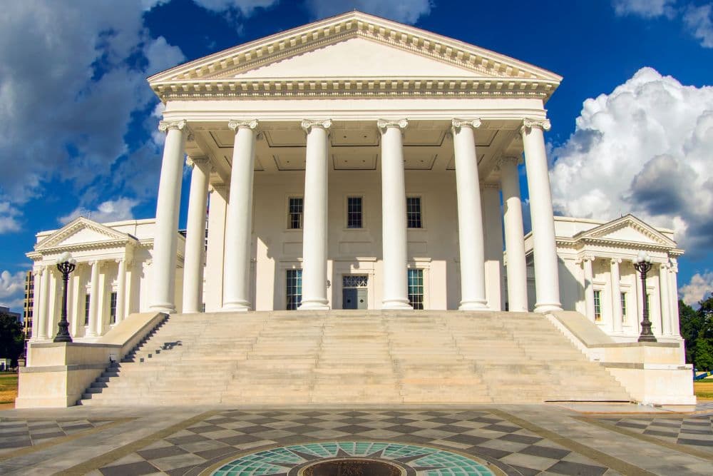 Front view of a classical building with large columns and steps under a blue sky.