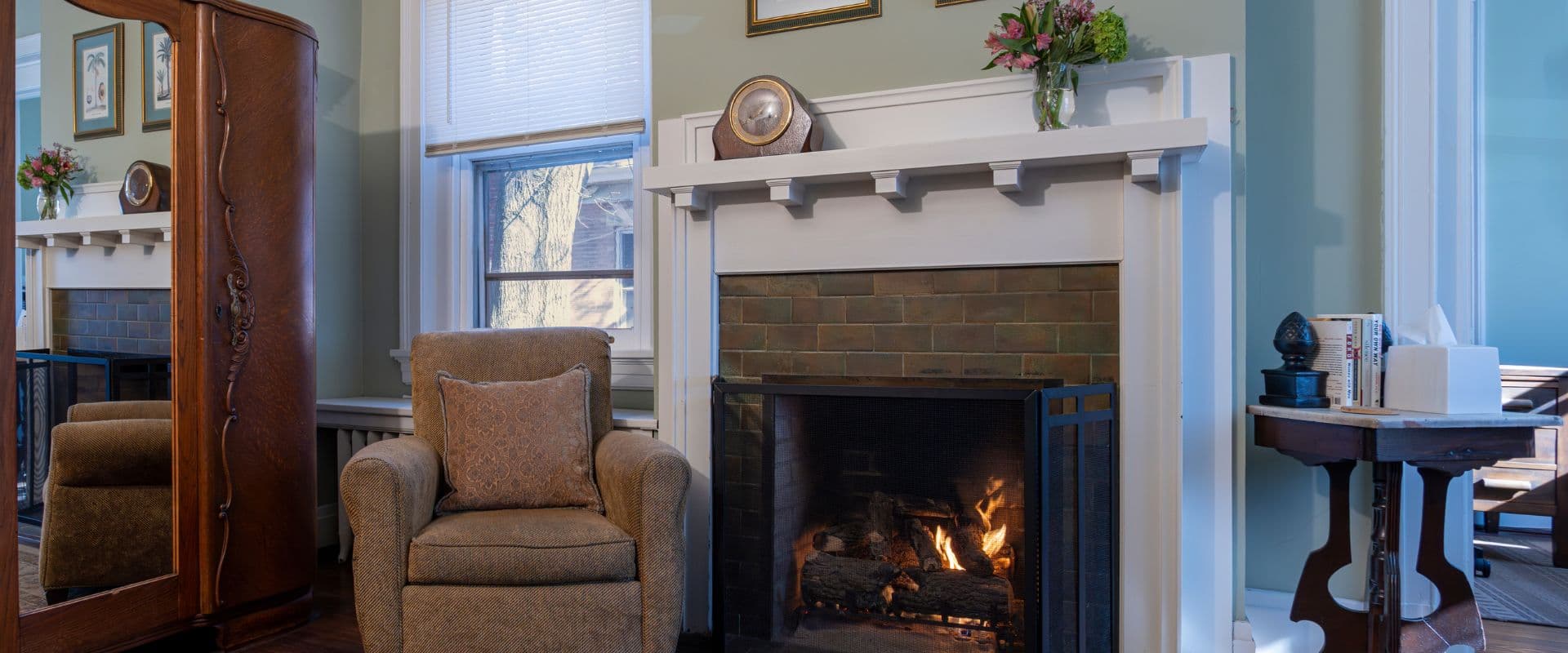Interior of a living room with fireplace, chair, mirrored armoire, side table